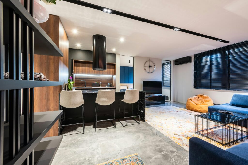 Modern kitchen and room interior with sofa against table and chairs under hood in light house